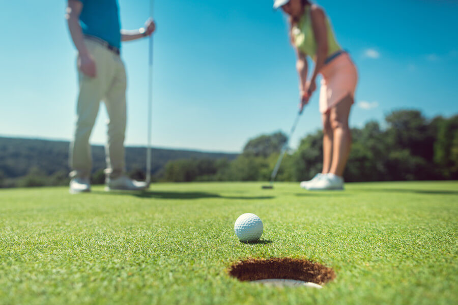 couple playing golf with the woman on green to hole